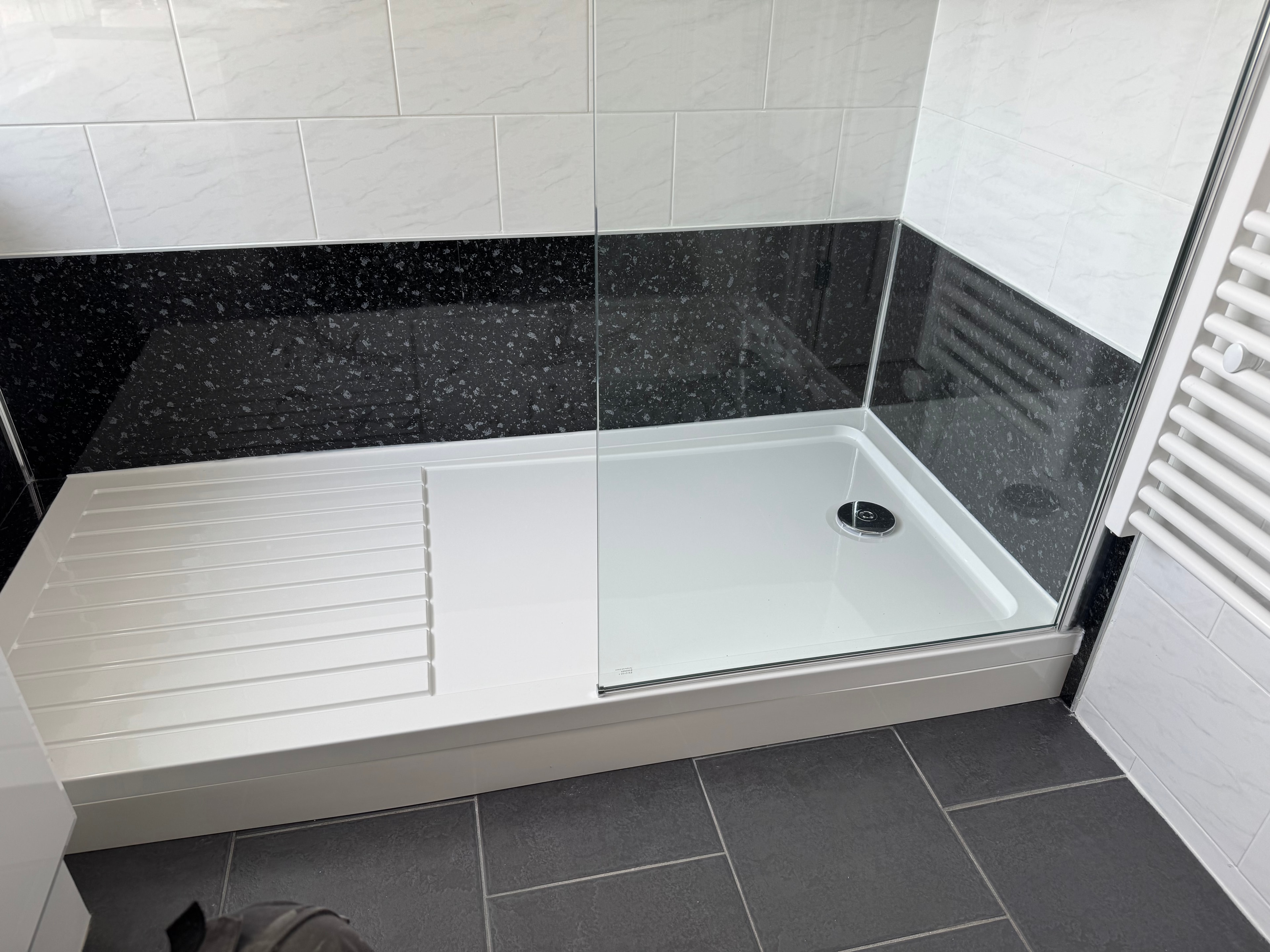 Shower tray with black granite splashback panels and glass screen