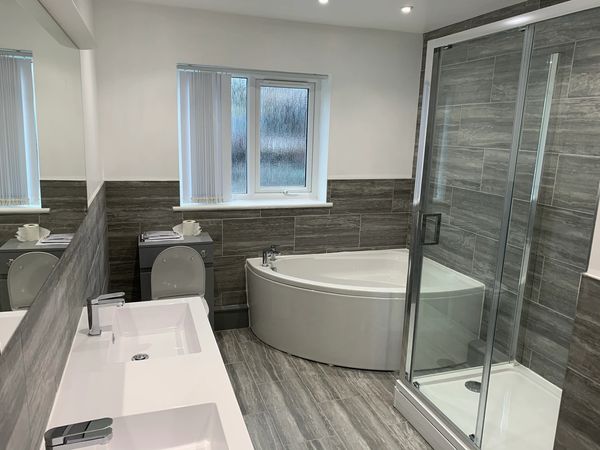 Bathroom complete — corner bath, sinks and shower cubicle with wall tiles